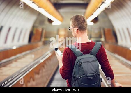 Traveling by public transportation. Young man listening music in headphones on the escalator to the subway. Stock Photo