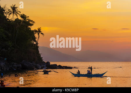 An outrigger canoe and crew makes its way to shore during a lovely sunset on White Beach at Puerto Galera, Mindoro Island, Philippines, Southeast Asia Stock Photo