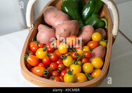 Fresh tomatoes, potatoes and green peppers in a trug and on display at a Horticultural Show. Stock Photo