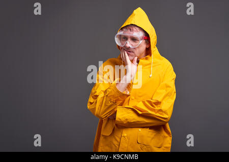 A middle aged man standing and thinking in a yellow raincoat Stock Photo