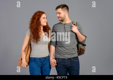 A beautiful young couple standing towards the camera while holding each others hands and bags on their shoulders Stock Photo