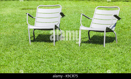 Two outdoor metal chairs stand on fresh green grass in summer park Stock Photo