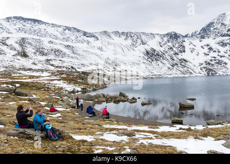 Hikers Taking a Break at Red Tarn Below Striding Edge, Helvellyn, Lake District, Cumbria UK. Stock Photo