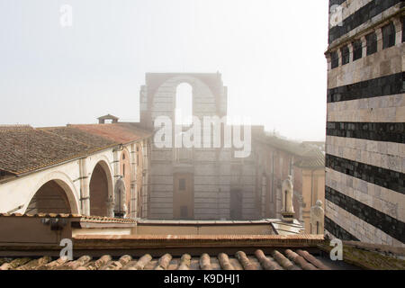 Italy, Siena - December 26 2016: the view of the tiled roofs and incomplete facade of the planned Duomo nuovo in fog. Facciatone on December 26 2016 i Stock Photo