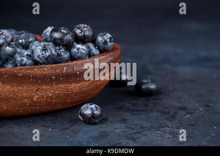 Fresh blueberries with a leaf of mint in the heart-shaped bowl on a dark blue background Stock Photo