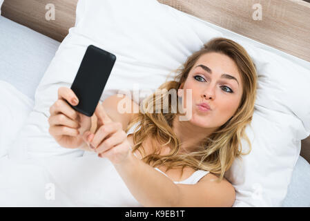 High Angle View Of A Young Woman Lying On Bed Taking Selfie Stock Photo