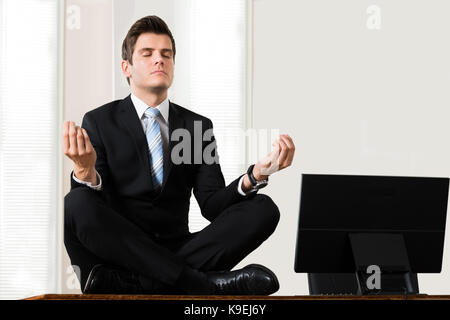 Young Businessman Sitting In Lotus Position Near The Computer At Desk Stock Photo