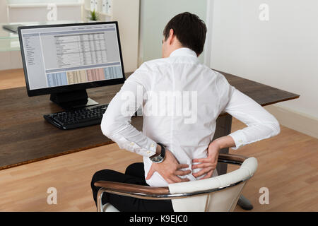 Young Businessman Sitting On Chair And Suffering From Backache At Desk Stock Photo