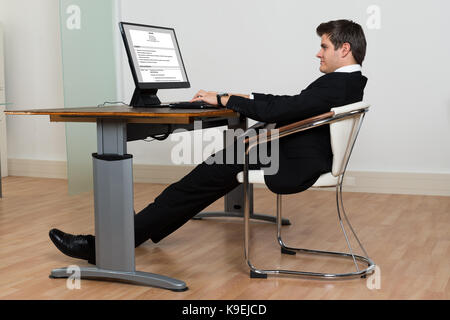 Businessman Leaning Back In His Chair While Working On Computer In Modern Office Stock Photo