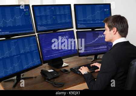 Young Businessman Working With Graphs On Six Computers At Desk Stock Photo