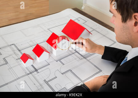Male Architect Looking At House Models On Blueprint Through Magnifying Glass Stock Photo