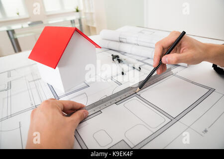 Close-up Of Engineer Drawing Diagrams In Front Of House Model On Blueprint Stock Photo