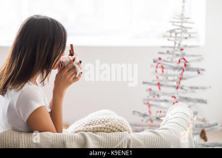 Young beautiful woman drinking hot chocolate with marshmallow in christmas decorated home. Holiday concept Stock Photo