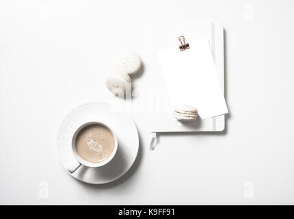 White flat lay with beige macaroons, coffee cup, notepad and postcard mockup on white table background Stock Photo