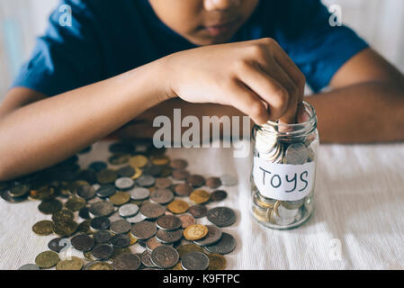 young asian boy putting coins into glass jar. Saving money to buy toys. Saving concept Stock Photo