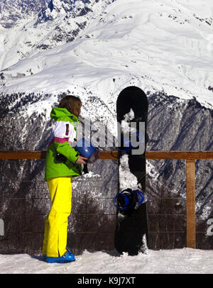 Young snowboarder with helmet in hands and snowboard on viewpoint in winter mountains at sun day. Caucasus Mountains. Hatsvali, Svaneti region of Geor Stock Photo
