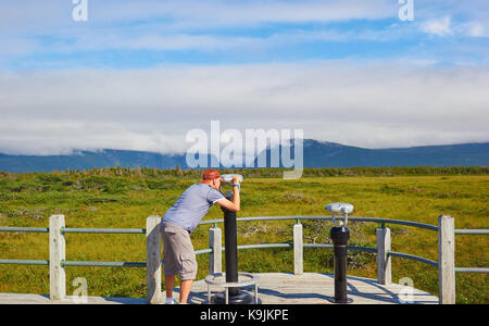 Male tourist looking through telescope at Western Brook Pond, a lake in the Long Range Mountains in Gros Morne National Park, Newfoundland, Canada Stock Photo