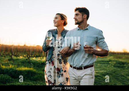 Man and woman with a drink walking outdoors. Couple together with a glass of wine in vineyard. Stock Photo