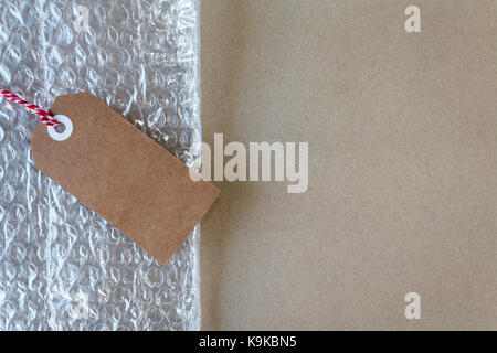 Postage and packaging materials with bubble wrap and a gift tag on brown wrapping paper with copy space Stock Photo