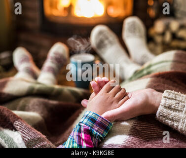 Warming and relaxing near fireplace. Mother and daughter holding hands in front of fire. Stock Photo