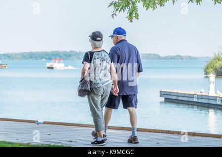 Senior couple walk hand in hand along the boardwalk at the waterfront in Orillia Ontario Canada. Stock Photo