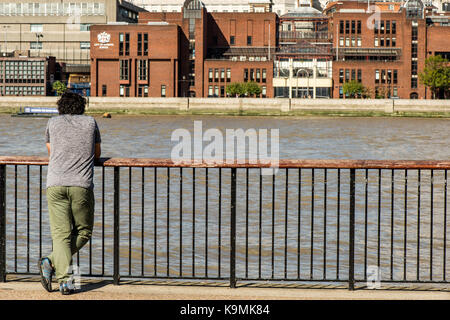 Man With His Back To The Camera Leaning on a Safety Fence Looking Across The River Thames in London United Kingdom in a Thoughtful Releaxed Pose, Wear Stock Photo
