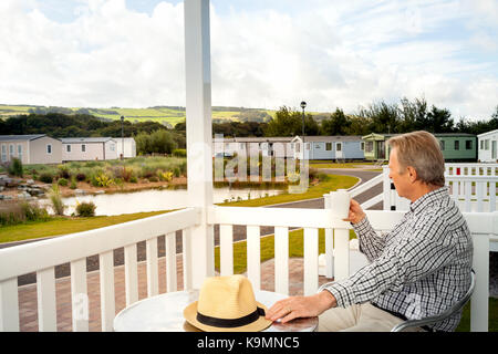 Elderly man drinking a mug of coffee sitting on the veranda of a luxury static caravan in North Wales taking in the scenic views of the Welsh  Country Stock Photo