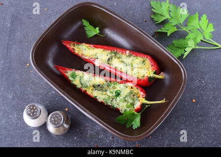 Oven cooked red paprika stuffed with cheese, garlic and herbs in a ceramic form on an abstract grey background. healthy eating concept. Mediterranean  Stock Photo