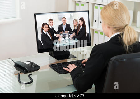 Young Businesswoman At Desk Video Conferencing With Colleagues On Computer In Office Stock Photo