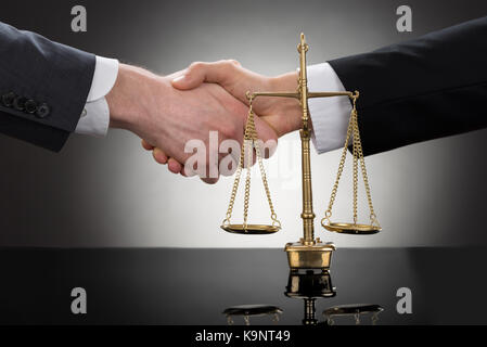 Close-up Of Two Businessman Shaking Hands In Front Of Scale Stock Photo