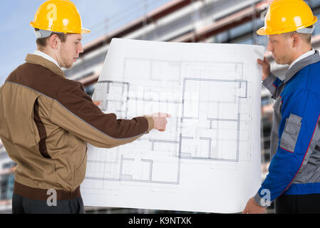 Two Architects At Construction Site Discussing Blueprint Stock Photo