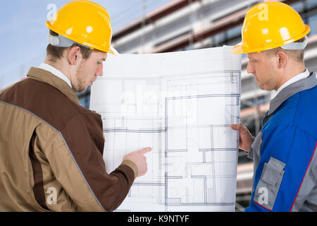 Two Architects At Construction Site Discussing Blueprint Stock Photo