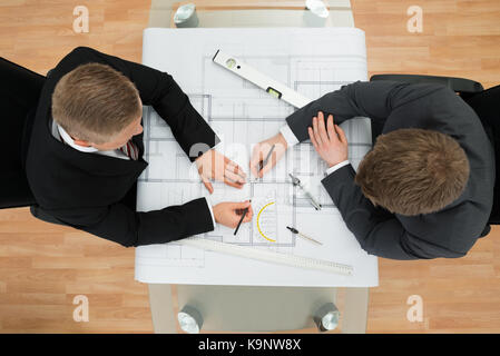 Elevated View Of Two Businessman Drawing Plan On Blueprint In The Office Stock Photo