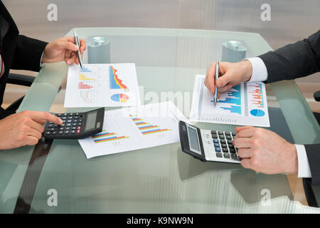 Close-up Of Two Businessmen Analyzing The Graph Using Calculator On Office Desk Stock Photo