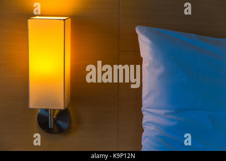 bedside lamp with its warm light turned on next to white bed and pillow at night with space for text or copy space, good for home at night concept Stock Photo
