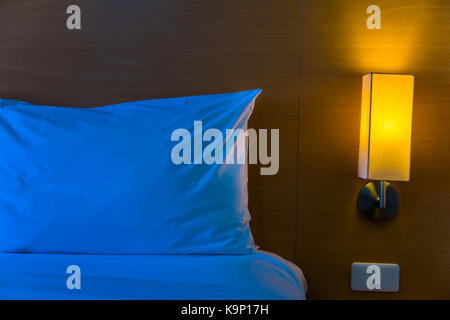 bedside lamp with its warm light turned on next to white bed and pillow at night with space for text or copy space, good for home at night or lonlines Stock Photo