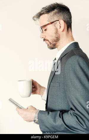 Side profile view portrait of professional businessman holding mobile phone and coffee mug wearing eye glasses. Stock Photo
