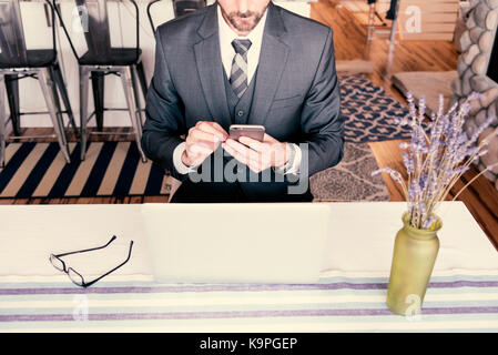 Man sitting at office table using a mobile phone to send a text message wearing a very nice suit with tie and vest. Stock Photo