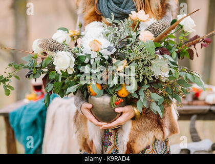 arranging, fall, style concept. girl wearing ornamental dress and fox jacket holding vase with wondreful autumnal bunch composed of various flowers and decorated with leaves of eucaliptus and rosebush Stock Photo