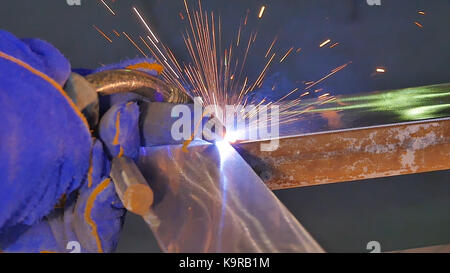Metal Welding with sparks and smoke. Worker with protective mask welding metal. Welder joins metal parts. A process using a semi-automatic welding. Welding steel. Industrial Worker at the factory welding closeup. Industrial welding automotive. Industy in slow motion Stock Photo