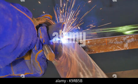Metal Welding with sparks and smoke. Worker with protective mask welding metal. Welder joins metal parts. A process using a semi-automatic welding. Welding steel. Industrial Worker at the factory welding closeup. Industrial welding automotive. Industy in slow motion Stock Photo
