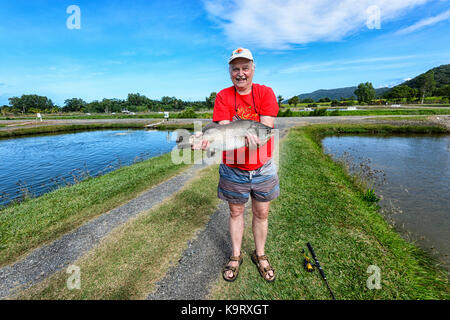 Fisherman holding a caught barramundi at a barramundi farm, Mossman, Far North Queensland, FNQ, QLD, Australia Stock Photo