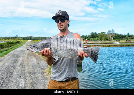Fisherman holding a caught barramundi at a barramundi farm, Mossman, Far North Queensland, FNQ, QLD, Australia Stock Photo