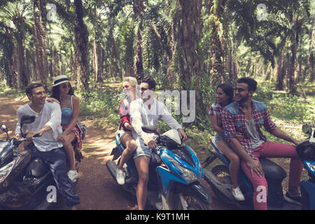 Young Group Of People Driving Scooters Travel In Tropical Forest Cheerful Friends Having Road Trip On Bikes Stock Photo