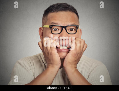 Closeup portrait headshot nerdy young guy with glasses biting his nails looking at you with craving for something or anxious isolated on grey wall bac Stock Photo