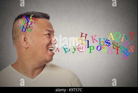 Side view portrait young handsome man talking with alphabet letters coming out of open mouth isolated grey wall background. Human face expression emot Stock Photo