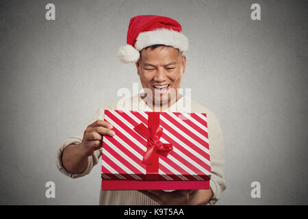 Closeup portrait happy excited surprised middle aged man opening unwrapping red gift box isolated grey wall background, enjoying his present. Positive Stock Photo