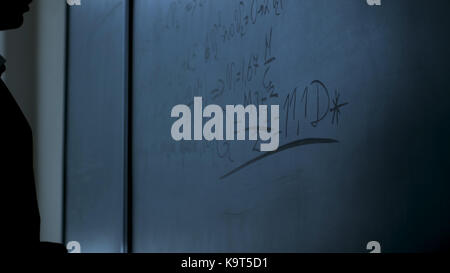 Scientist writing formulas on chalkboard. Hand with chalk wrote physics formulas on black chalkboard closeup Stock Photo