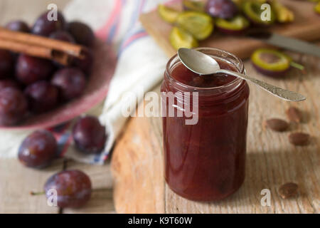 Homemade plum jam or confiture in a glass jar, and fresh plums on a wooden background. Rustic style, selective focus. Stock Photo