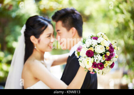 young asian newly wed couple hugging each other during wedding ceremony, focus on the bouquet. Stock Photo